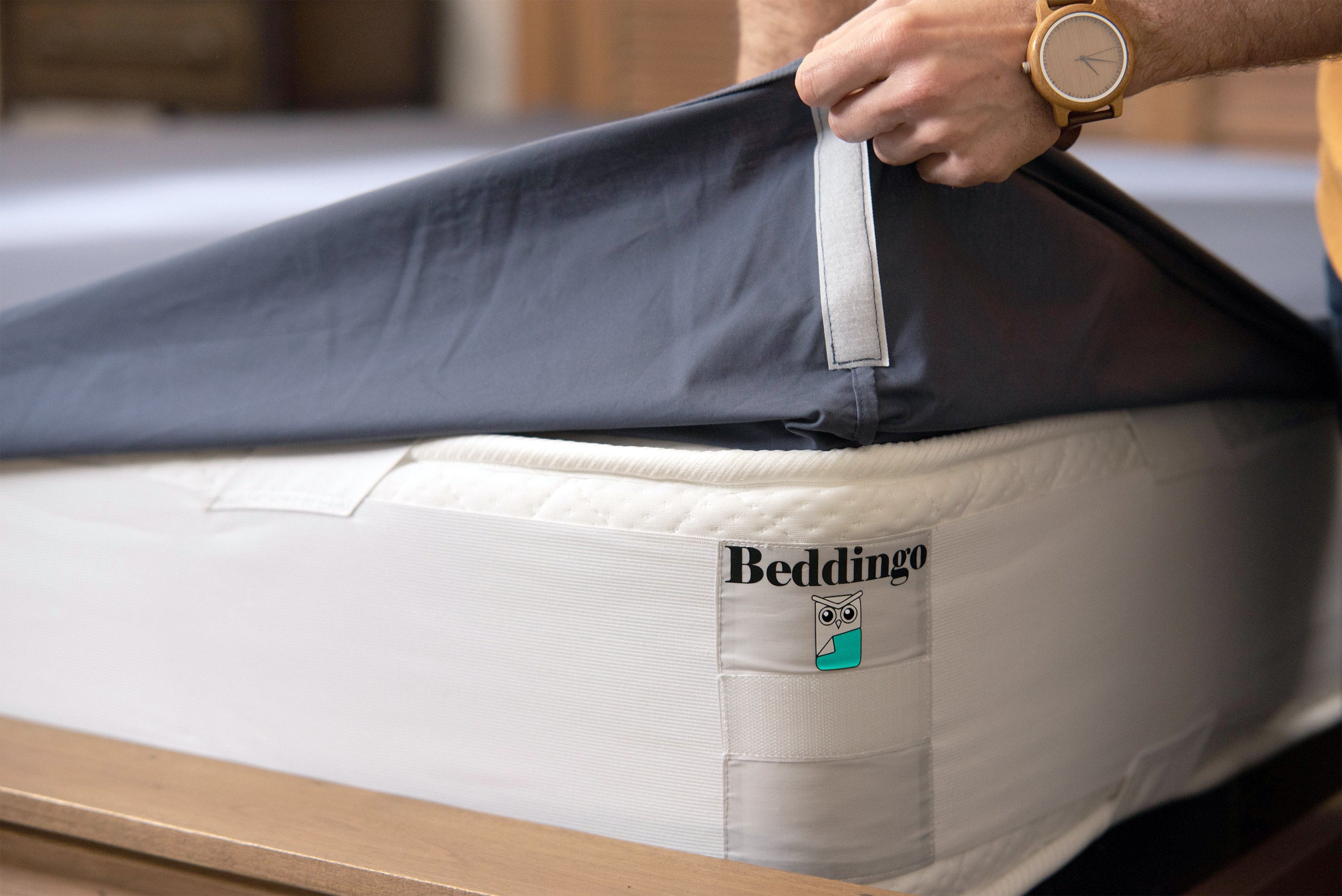 Person holding Beddingo bed sheet with velcro - going to attach to bed corner velcro with Beddingo logo